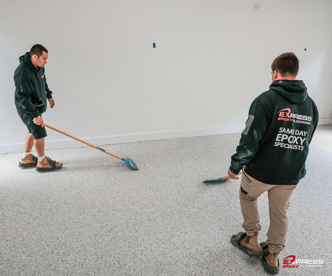 Two workers applying epoxy flooring with rollers in a room, wearing branded Express Epoxy Flooring hoodies.